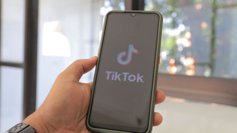 Close-up of a hand holding a smartphone with the TikTok app on screen in a bright indoor setting.