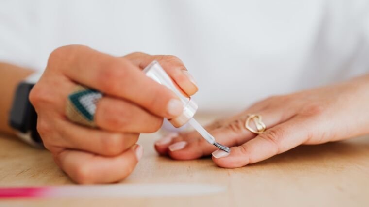 A close-up of a woman applying clear nail polish for a neat manicure.