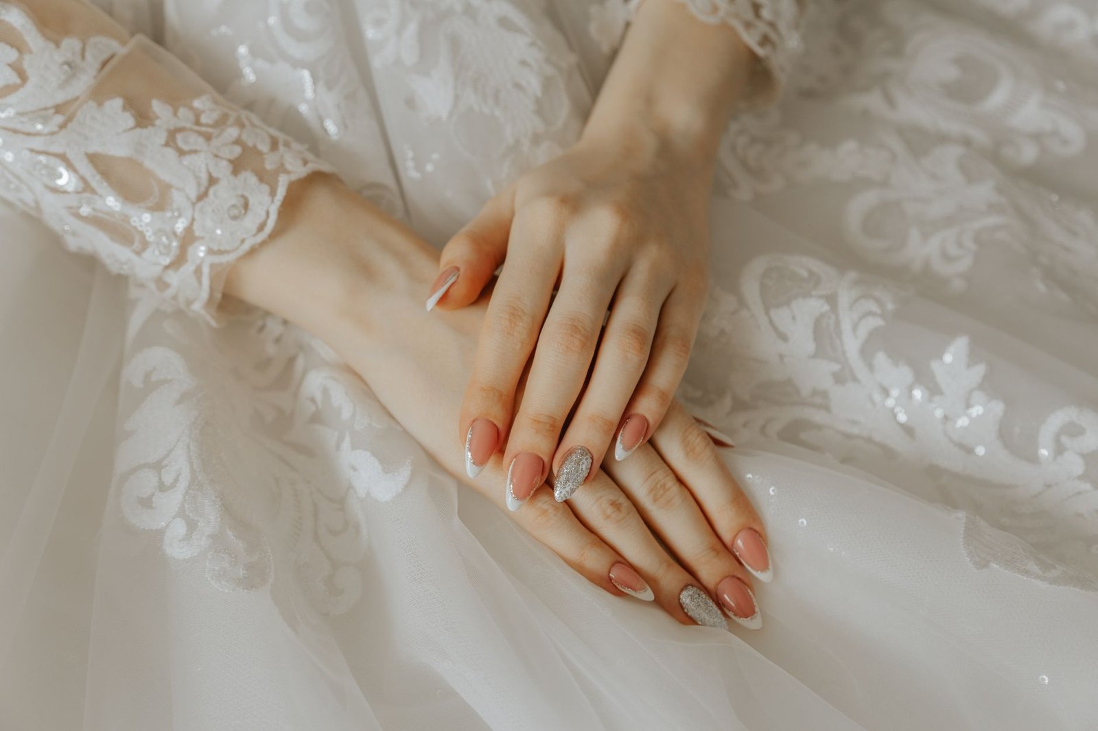 Close-up of a bride's hands on a detailed lace wedding dress, highlighting elegance and beauty.