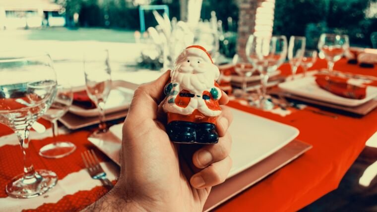 Hand holding a Santa Claus figurine at a festive outdoor table setting, perfect for Christmas celebrations.