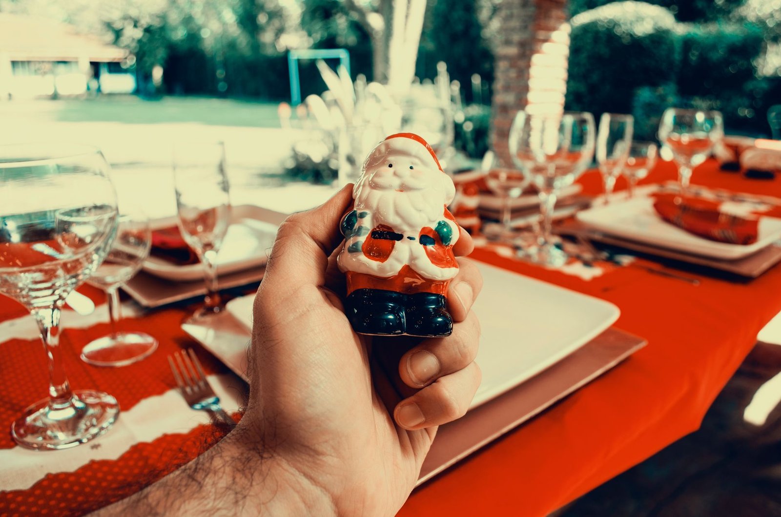 Hand holding a Santa Claus figurine at a festive outdoor table setting, perfect for Christmas celebrations.