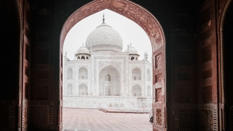 View of the iconic Taj Mahal through a decorative arched doorway, highlighting its architectural brilliance.