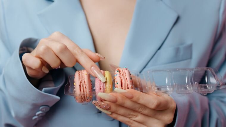Close-up of hands holding colorful French macarons, highlighting manicured nails.