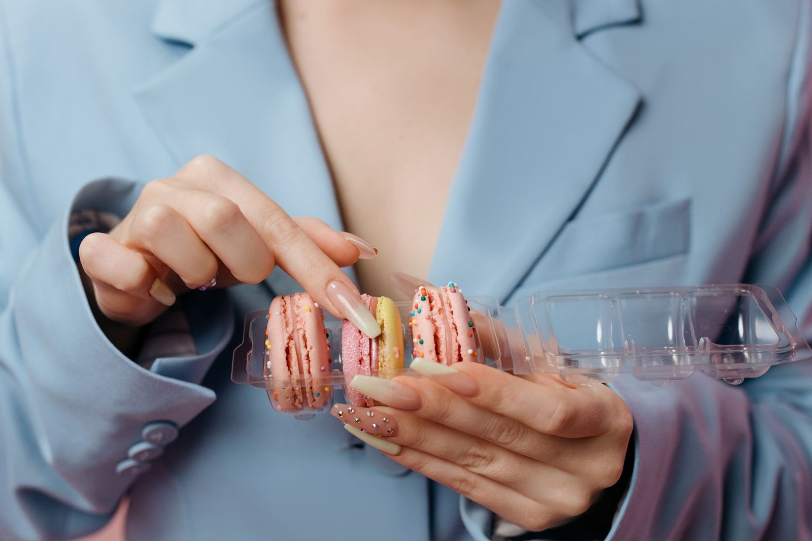 Close-up of hands holding colorful French macarons, highlighting manicured nails.