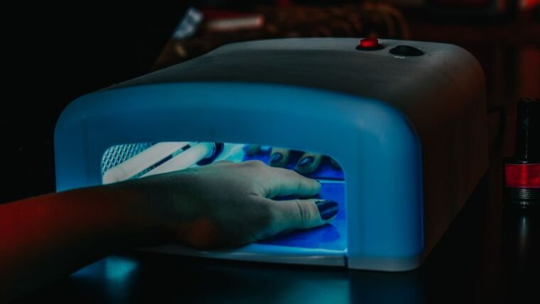 A hand with manicured nails being cured under a blue LED lamp for gel polish.