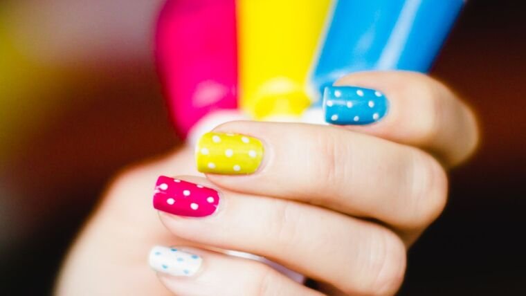 Close-up of colorful polka dot nail art on hand, showcasing pink, yellow, and blue shades.