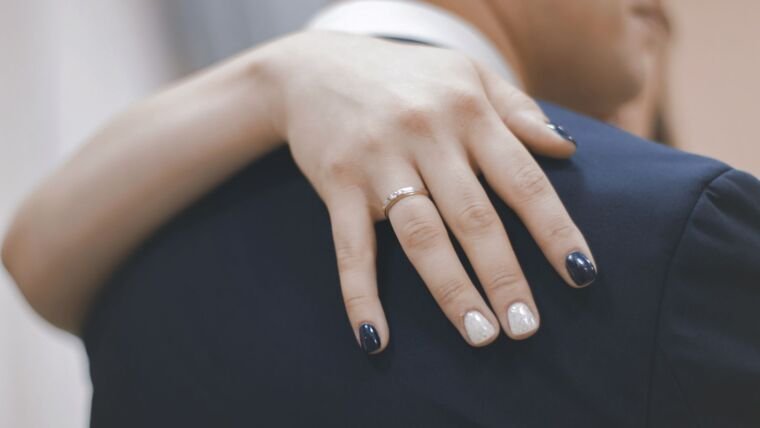 Close-up of a hand with diamond engagement ring resting on partner's shoulder, symbolizing love.