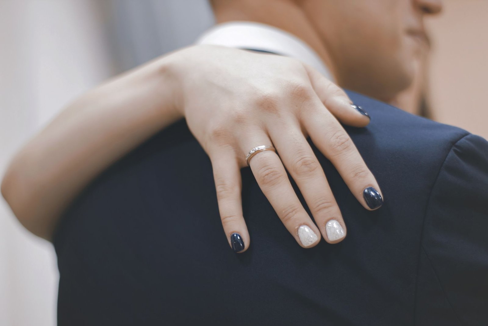 Close-up of a hand with diamond engagement ring resting on partner's shoulder, symbolizing love.