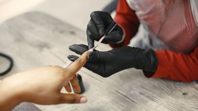 A nail artist carefully applies nail polish to a client's nails in a salon setting, using precise techniques.